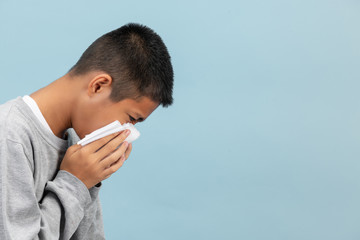 A boy is sneezing into tissue and feeling sick on blue background.