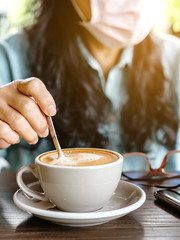 Woman with medical face mask drinking coffee in her house alone during corona virus or COVID-19 quarantine, Physical distancing for protect Covid-19 concept. Selective focus.