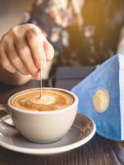 Woman with medical face mask drinking coffee in her house alone during corona virus or COVID-19 quarantine, Physical distancing for protect Covid-19 concept. Selective focus.
