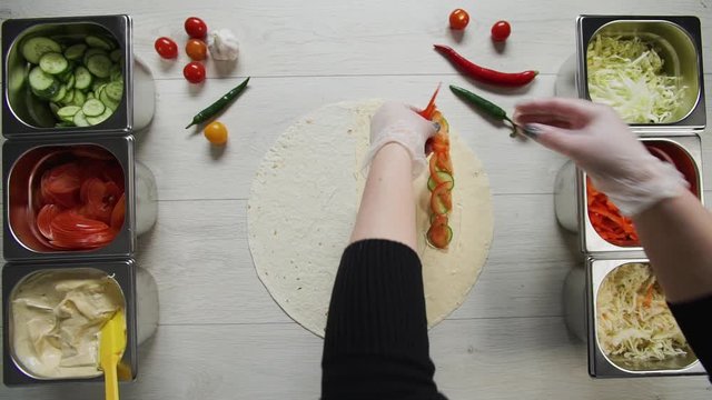 Top view of chef hands in white gloves puts peppres on doner kebab shawarma in pita or lavash. Shawarma with chicken cutlet, pappers, cheese and vegetable