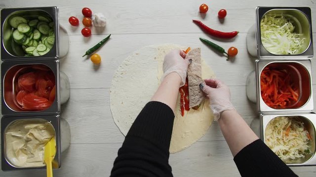 Top view of chef hands in white gloves puts beef cutlet on doner kebab shawarma in pita or lavash. Shawarma with beef cutlet, pappers, cheese and vegetable