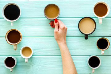 Coffee addiction. Mug in hand, many cups on green wooden desk top-down