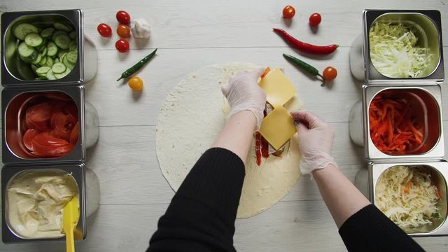 Top view of chef hands in white gloves puts cheese on doner kebab shawarma in pita or lavash. Shawarma with beef cutlet, pappers, cheese and vegetable