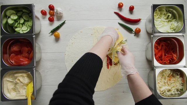 Top view of chef hands in white gloves puts cabbage on doner kebab shawarma in pita or lavash. Shawarma with chicken cutlet, pappers, cheese and vegetable