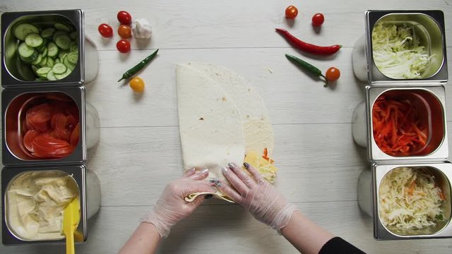 Top view of chef hands in white gloves wraps doner kebab shawarma in pita or lavash. Shawarma with chicken cutlet, pappers, cheese and vegetable