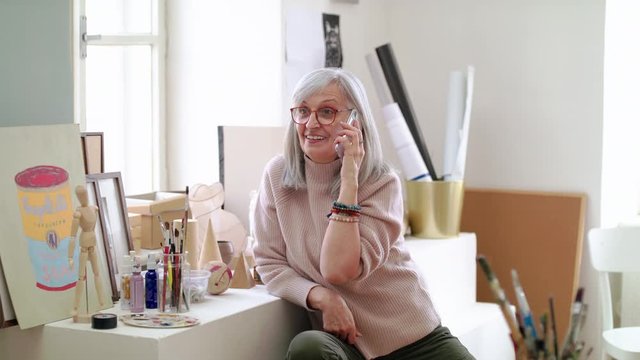 Senior woman with smartphone making phone call in art class.