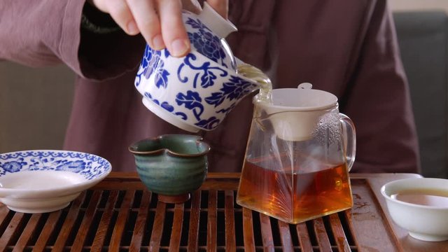 Tea master pouring fresh brewing tea from gaiwan into sieve to glasses jug. Man pouring hot tea beverage to glasses teapot on chaban tray while traditional chinese tea ceremony