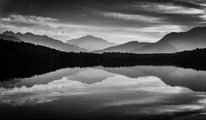 Monochromatic symmetrical reflections of layer of hills, forest and sky on the surface of Rara Lake in Nepal. 