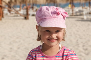 Portrait of little smiling girl in pink cap on sea beach background