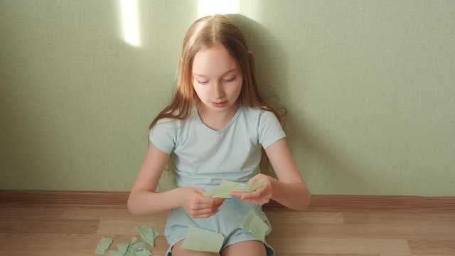 Sad girl tearing toilet paper to small pieces sitting at floor during self-isolation quarantine. Unhappy girl teenager tearing green toilet paper at home floor