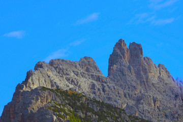 Beautiful Dolomites in Italy. Clear day with blue sky. Part of the mountains is covered with green vegetation. Selective focus.