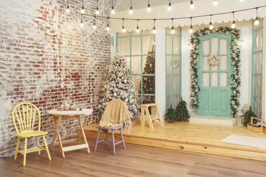 Porch of house with Christmas decorations. Retro street garland with light bulbs over the terrace of house. Garden table and chairs on the winter terrace background of Christmas trees - Powered by Adobe