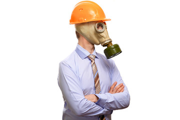 The protected businessman in a gas mask, construction helmet, shirt and tie crossed his arms on his chest, looks to the side. Isolated
