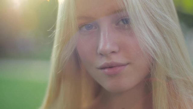 Close-up portrait of a beautiful caucasian blue-eyed blonde girl in the afternoon park. Young sexy teenage fashion model with healthy silky hair, clean skin posing in the sun and smiling.