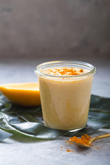 Yellow mango yogurt or smoothie on grey background. Turmeric Lassie or lassi in glass.