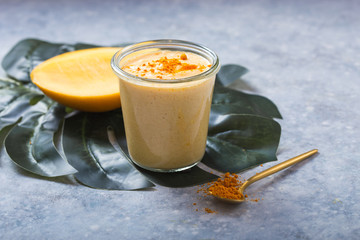 Yellow mango yogurt or smoothie on grey background. Turmeric Lassie or lassi in glass.
