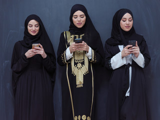 muslim women using mobile phone in front of black chalkboard