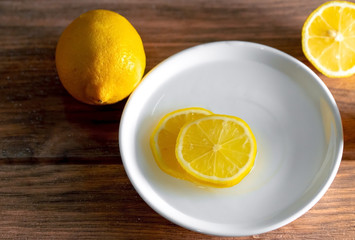 limón amarillo con cortes de limon en un plato de ceramica blanca vista desde arriba sobre una madera