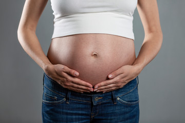 Big belly of a pregnant woman on a faithful background. Pleasant expectation. Close-up.