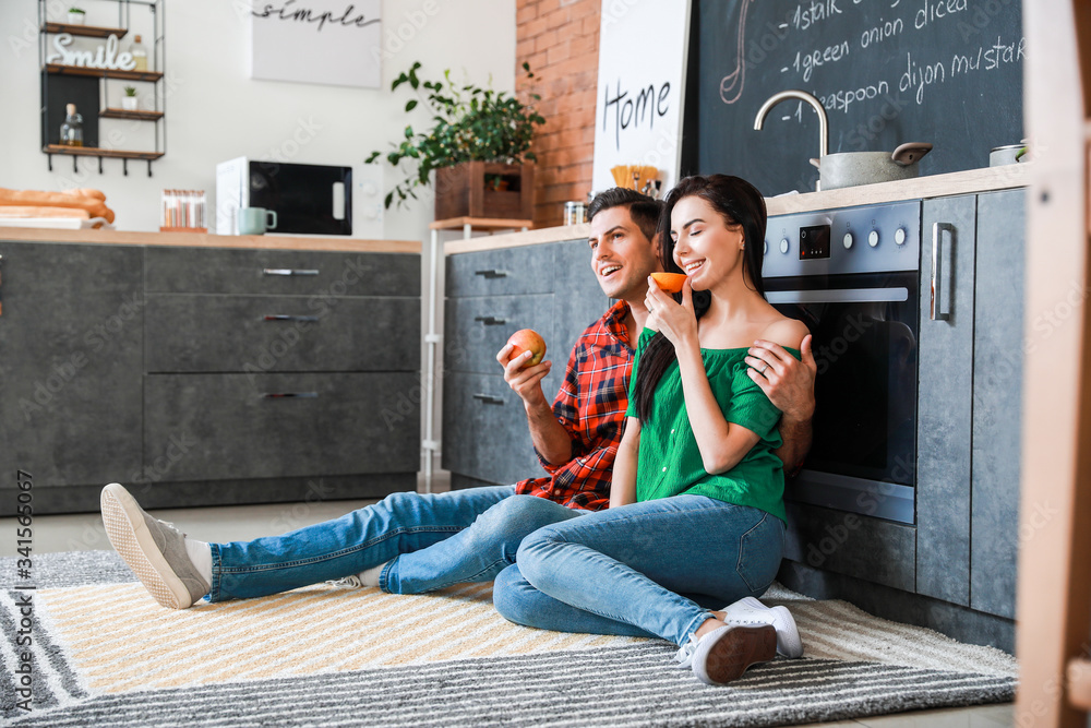 Wall mural Happy young couple eating fruits in kitchen