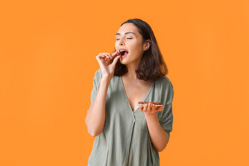 Beautiful young woman eating tasty chocolate candies on color background