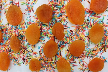 Decorative sprinkles border and dried apricots on white background. Multicolor Sugar confectionery powder and dried apricots in the corner. Scattered sweet sugar sticks and balls. Copy space.