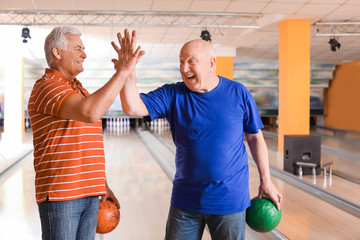 Portrait of senior men giving each other high-five in bowling club