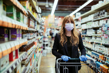 Woman in a face mask wearing latex gloves while shopping in a supermarket during coronavirus...