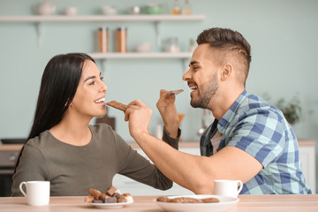 Beautiful young couple eating chocolate in kitchen