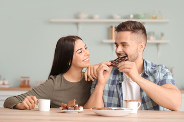 Beautiful young couple eating chocolate in kitchen