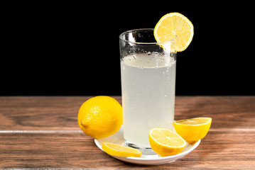 Un vaso de limonada fría con rebanadas de limón amarillo en un plato de color blanco