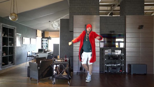 Young unusual guy funny dressed in a red coat with a gold chain around his neck and shorts, he fools around at home in self-isolation and therefore entertains himself and the TikToks audience