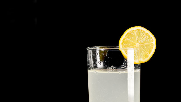 Un vaso de limonada fr&iacute;a con un pedazo lim&oacute;n amarillo con fondo de color negro primer plano