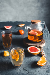 Citrus tea in a transparent teapot on a gray concrete background. Healthy drink, vegan, eco product.