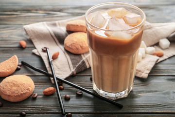 Glass of tasty iced coffee with cookies on wooden background