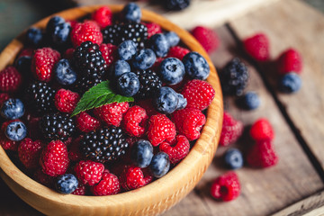 blueberries and raspberries, blackberry in a wooden bowl on old wood background