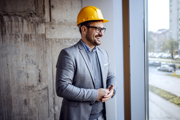 Smiling satisfied handsome architect standing in building in construction process and looking...
