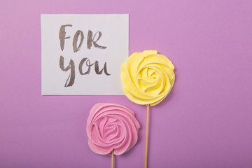 yellow and pink Rose candy   in pastel colors on a wooden stick with card "for you" on a color  background, Valentine, Mother's Day.
