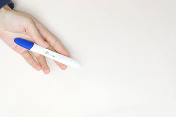 Woman hand holding a positive pregnancy test on pink background.
