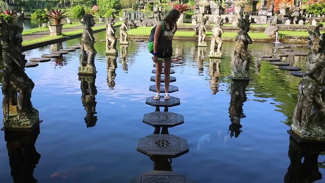 Slowmotion shot of a young woman tourist visiting the Tirta Gangga water palace, former royal palace on the Bali Island, Indonesia