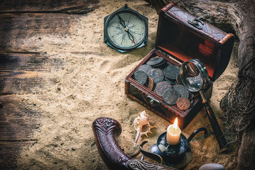 Pirate treasure chest with ancient coins and other various pirate equipment on table background.