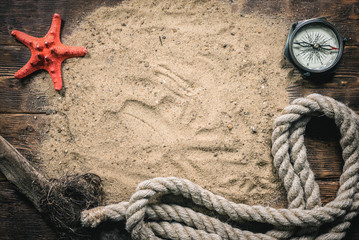 Red starfish, compass, mooring rope on the sand on wooden flat lay background with copy space.