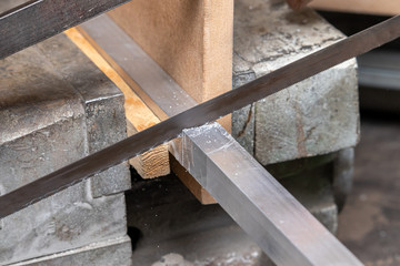 A man saws a square aluminum pipe clamped in a Vice with a hacksaw on metal