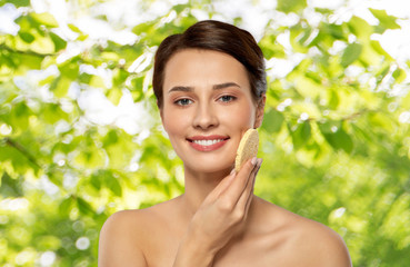 beauty, people and skincare concept - young woman cleaning face with exfoliating sponge over green natural background