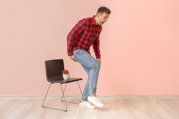 Young man and chair with cactus near color wall. Hemorrhoids concept