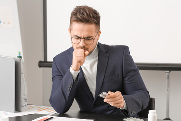 Ill young man taking medicine in office