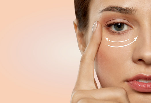 beauty, makeup and lifting concept - close up of beautiful young woman face with arrows under eye area over beige background