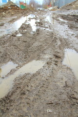 Dirty dirt road with track, wheel marks, brown clay and puddles in Russia.