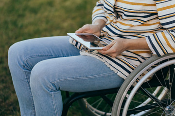 Fashionably dressed woman in a wheelchair with a modern tablet in hand walks on the street.