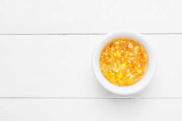 Bowl of fish oil capsules on white wooden background